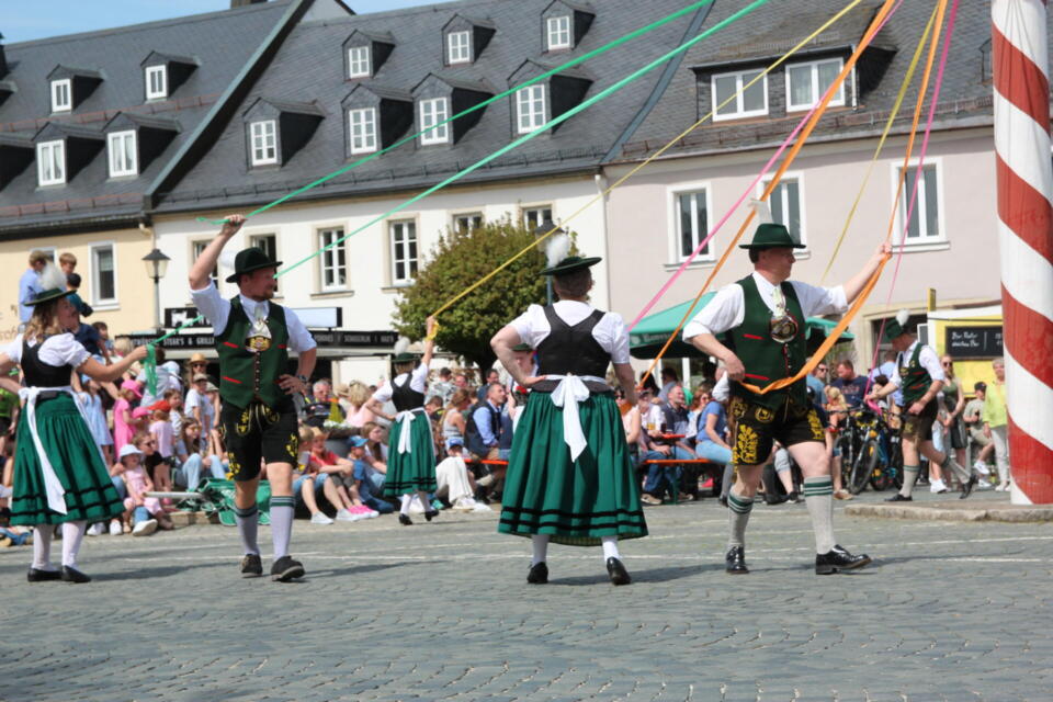 Menschen in Tracht tanzen um den Maibaum